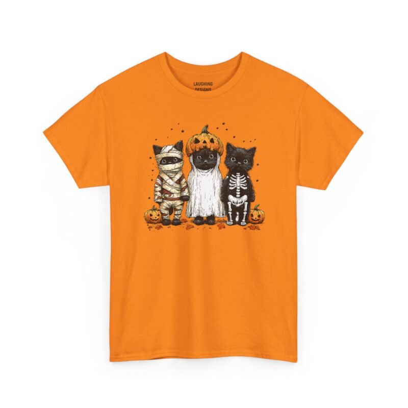 Funny t-shirt with three black kittens dressed up for Halloween; one wrapped as a mummy, one wearing a ghost sheet with a jack-o'-lantern on its head, and one in a skeleton costume, surrounded by autumn leaves, small stars, and pumpkins, printed on a Safety Orange color cotton shirt.