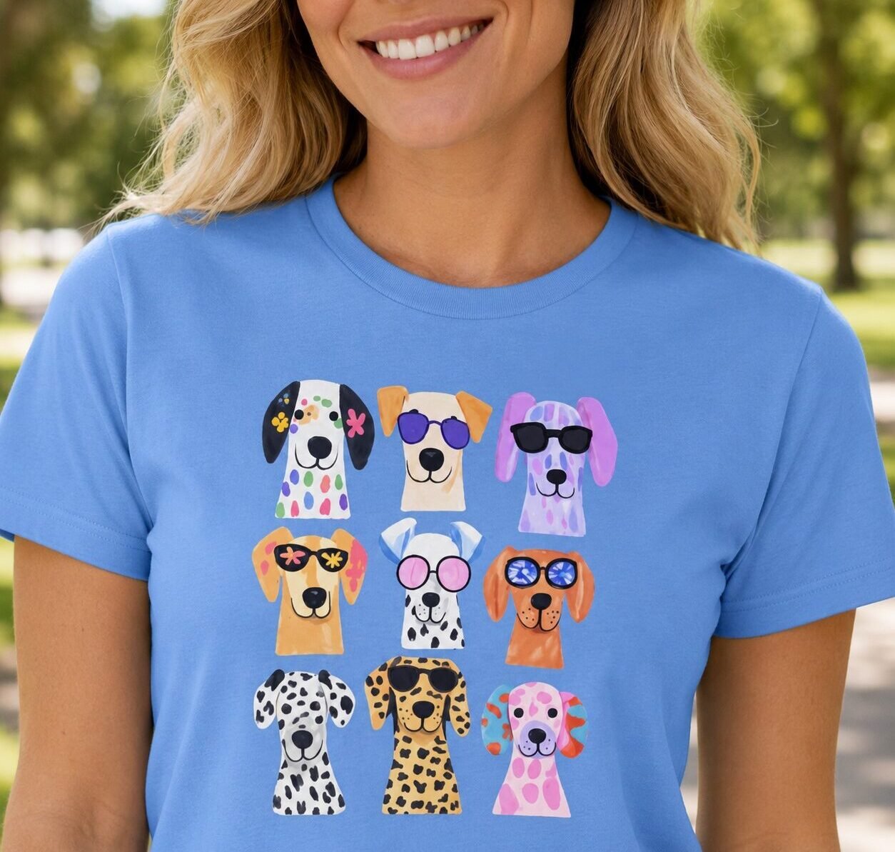 Cute Dogs T-shirt by Laughing Designs, female model wearing a Carolina blue shirt with a grid of colorful watercolor dogs wearing sunglasses.